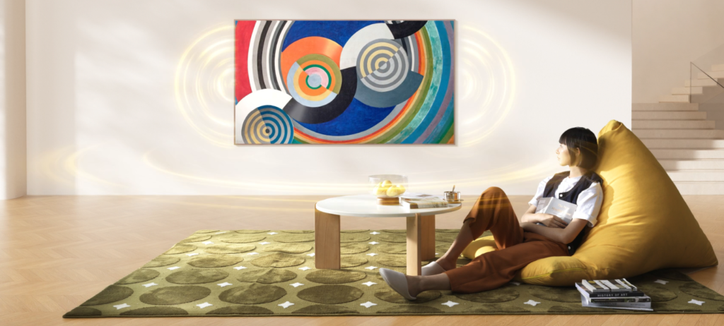image | TCL Kenya Woman relaxing on a yellow bean bag in a bright living room, reading a magazine beside a round white coffee table and bold abstract wall art.