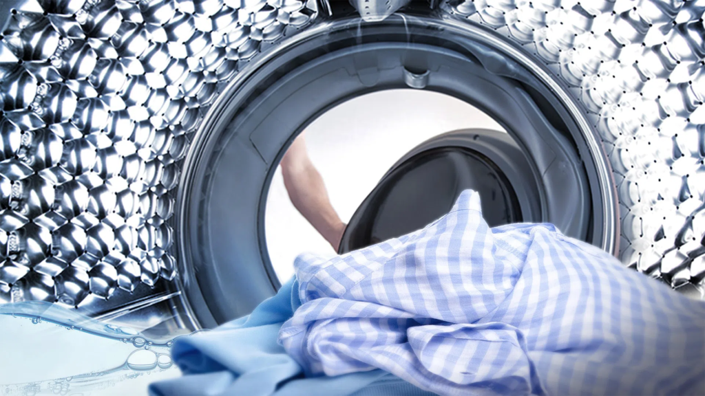 Person loading a blue and white checkered shirt into a front-loading washing machine drum.